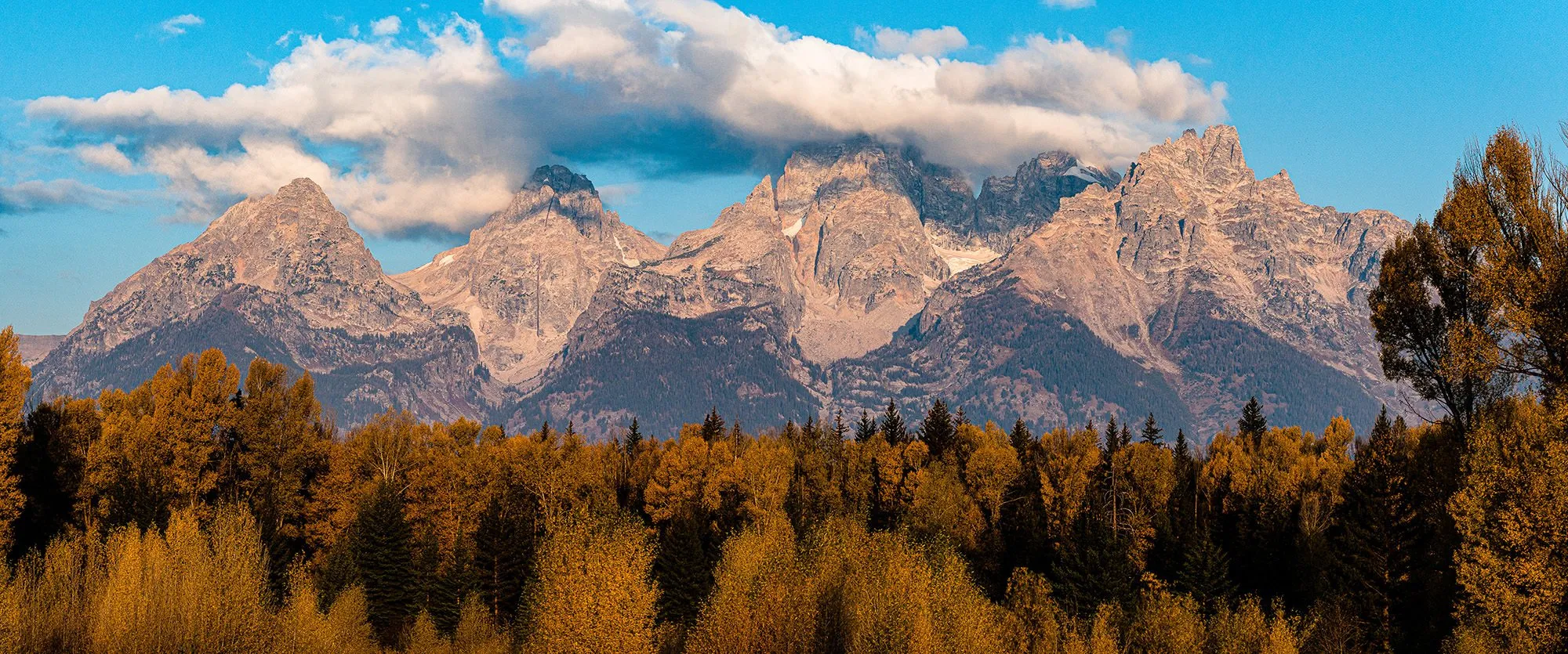 Panorama of rugged mountain peaks in clouds above an autumn forest.