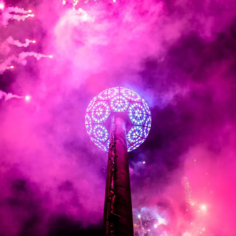 The Times Square New Year's Eve ball lit purple and blue among smoke and fireworks.