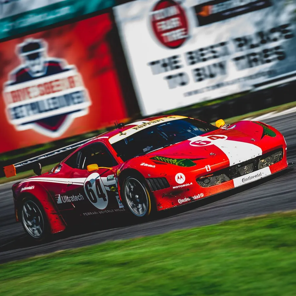 Red Ferrari race car number 64 with white stripe speeding on a racetrack, featuring sponsor logos including Motorola, Continental, and Ultratech, with blurred advertising billboards in the background.