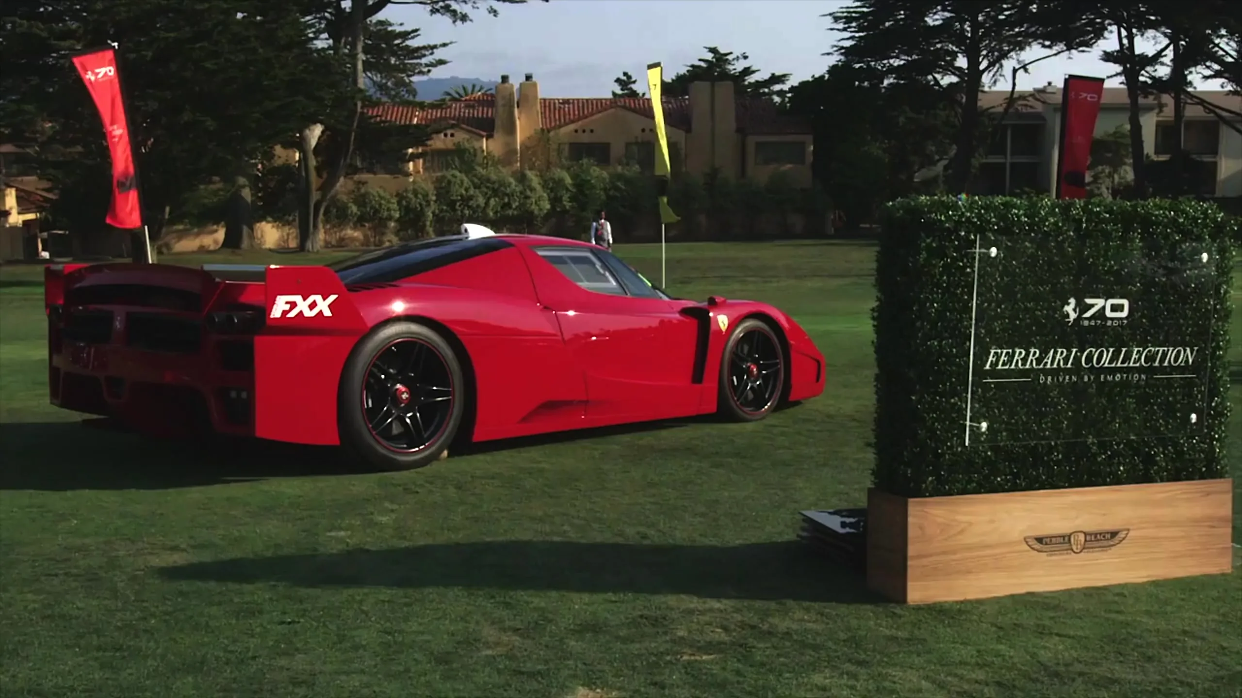 A red Ferrari FXX on the lawn at Pebble Beach beside the Ferrari 70th anniversary collection sign.