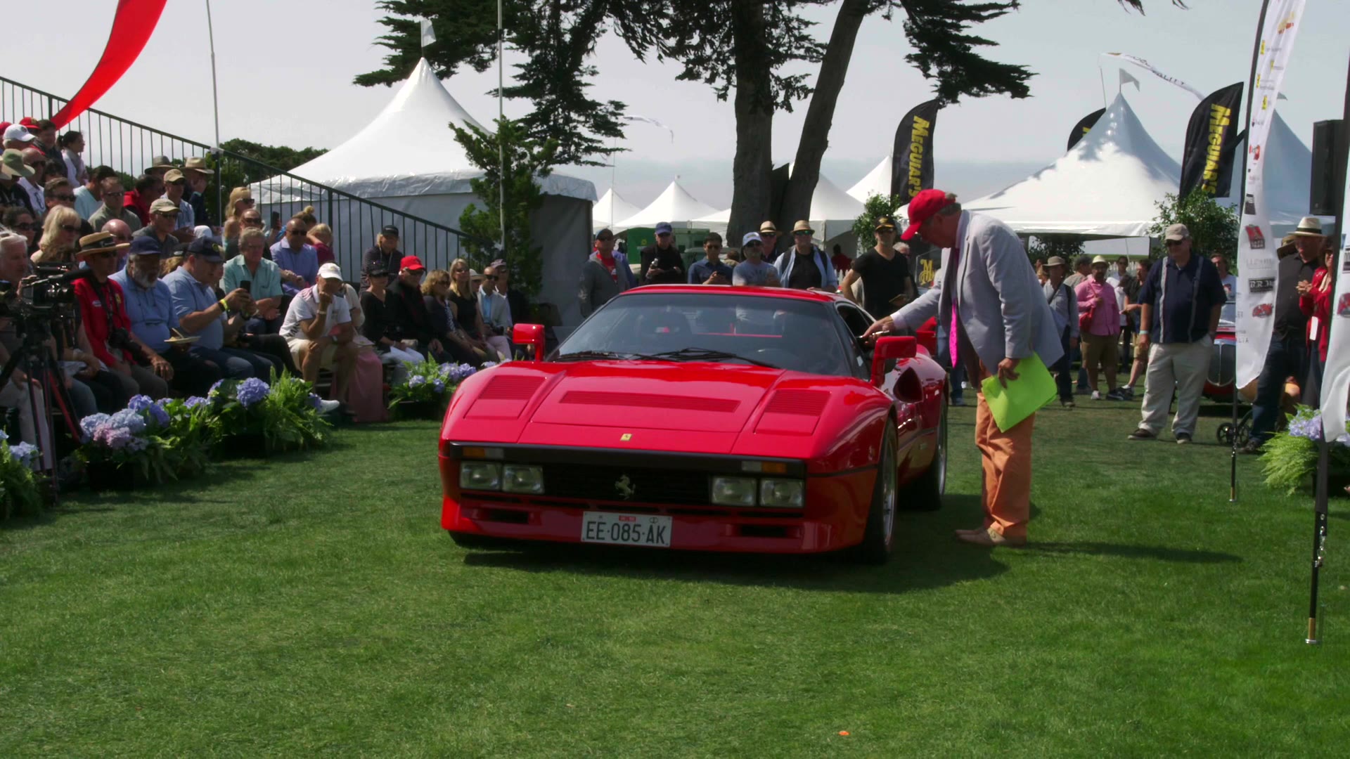 A red Ferrari on the lawn at Pebble Beach in front of a packed grandstand.