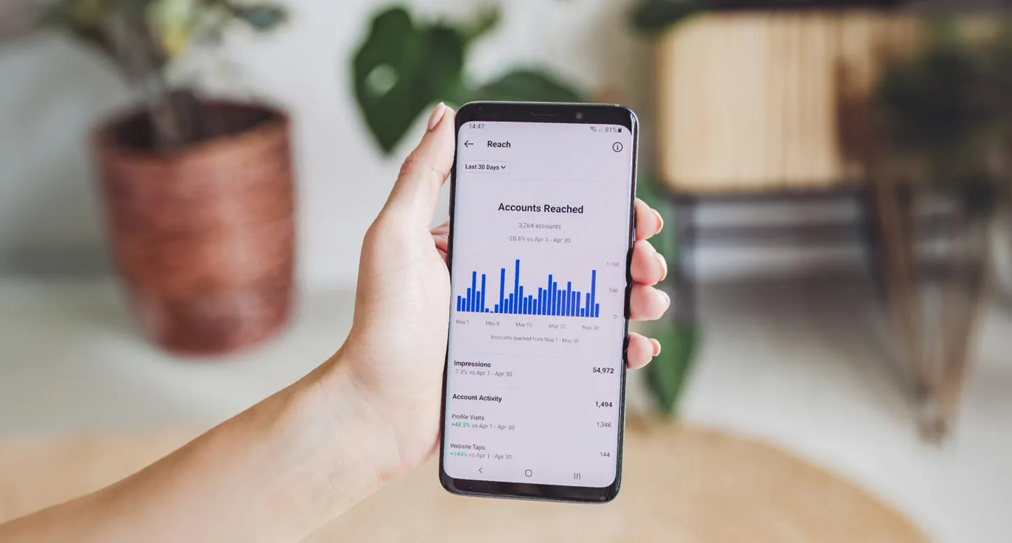 A hand holding an iPhone that shows e-commerce analytics for accounts reached in the last 30 days