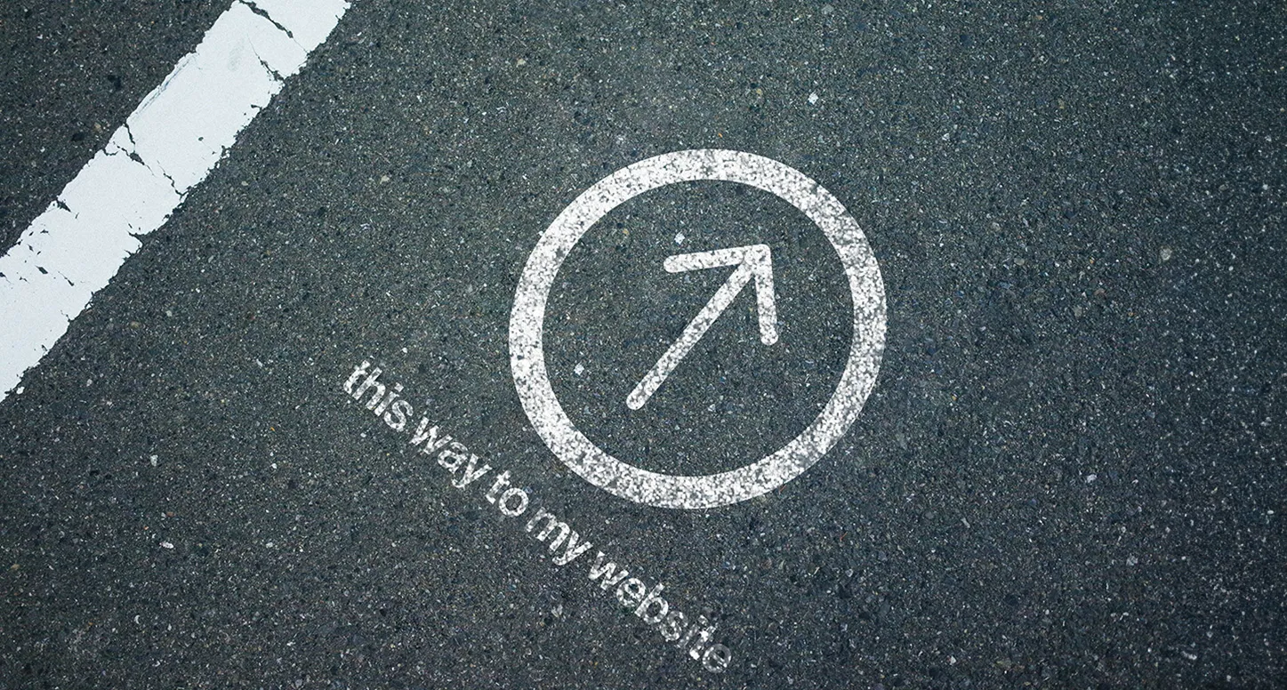 An arrow in a circle and "this way to my website" on asphalt
