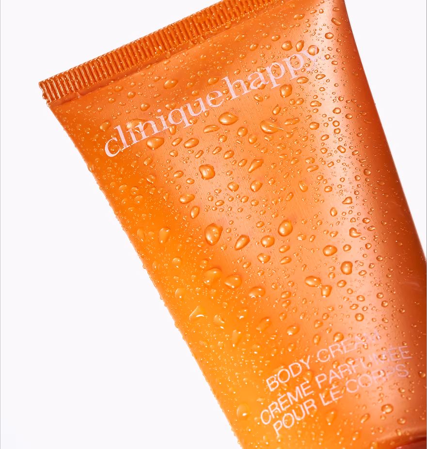 Orange Clinique Happy body cream tube with water droplets on its surface against a white background.