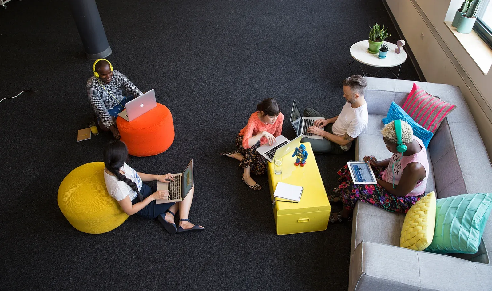 A team collaborating on laptops in a colourful lounge, seen from above
