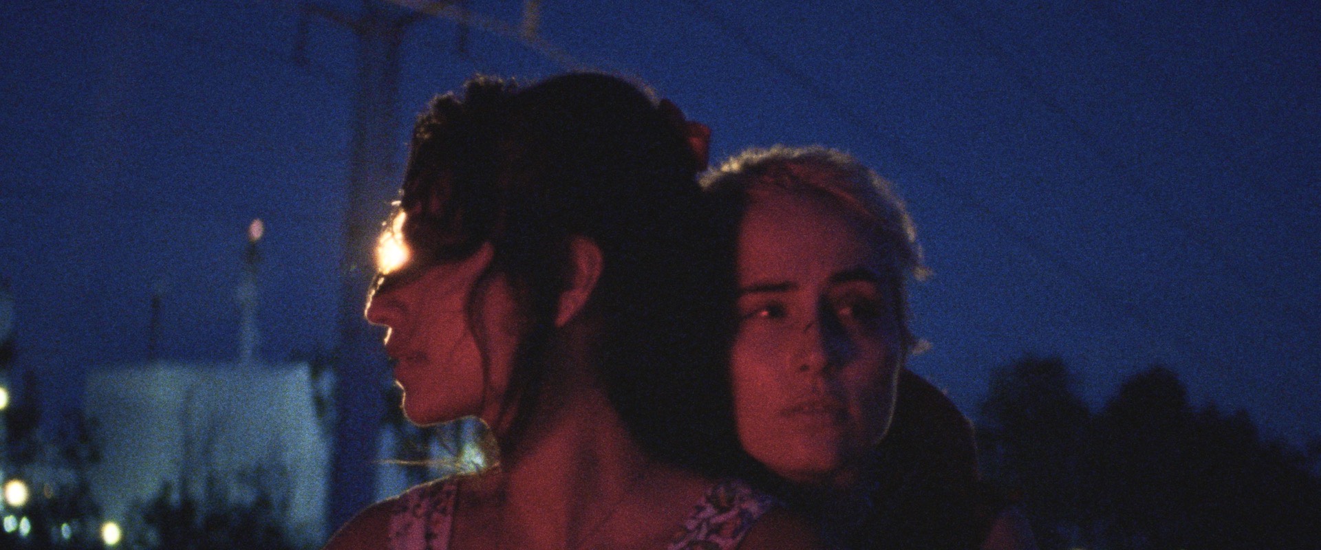 Annapurna Sriram and Sadie Scott leaning against each other outdoors at night under dim lighting.