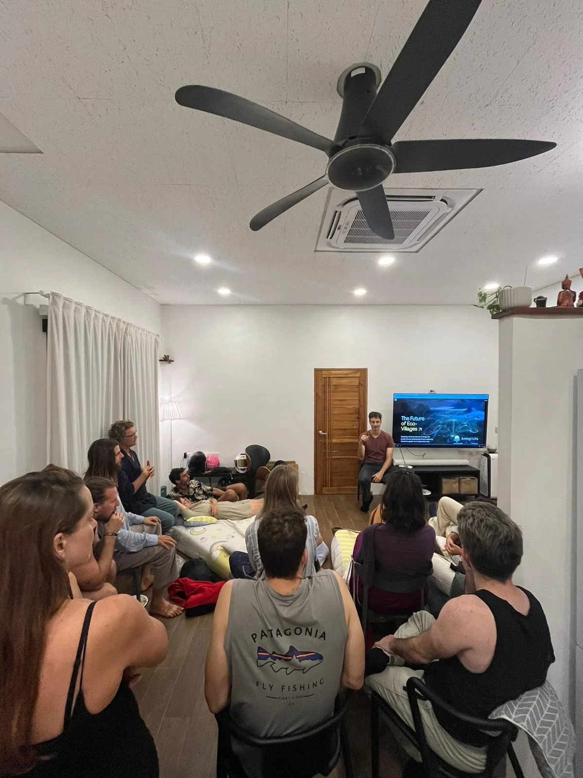 Friends sitting on mattresses in a living room, listening to a talk about eco-villages