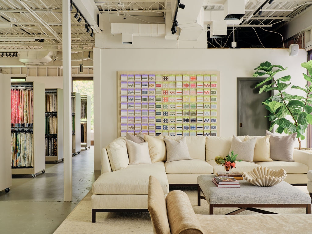 Showroom seating area with a cream sectional, plants and a wall of fabric samples
