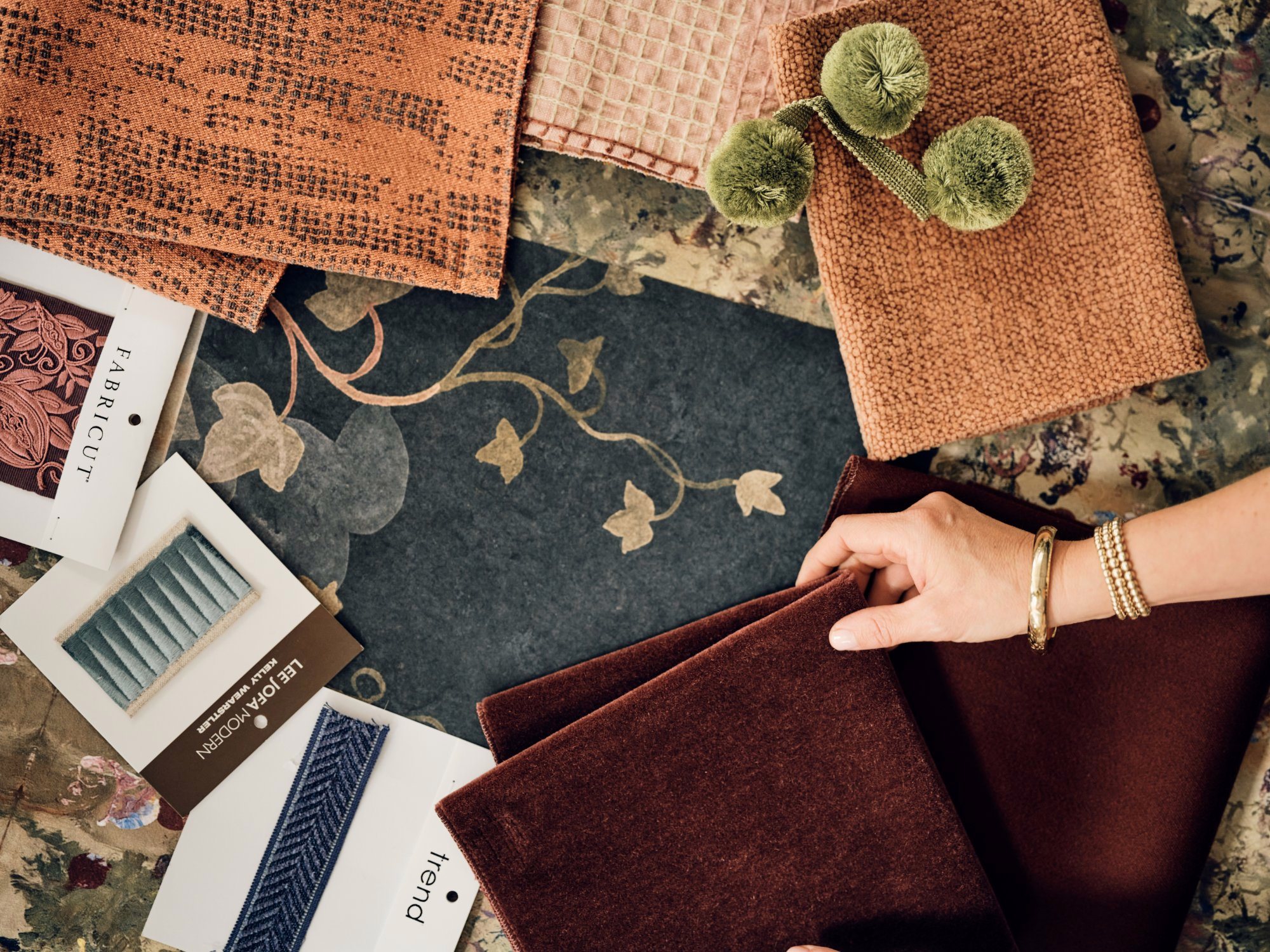 Hands layering a burgundy velvet swatch over rust and green textile samples