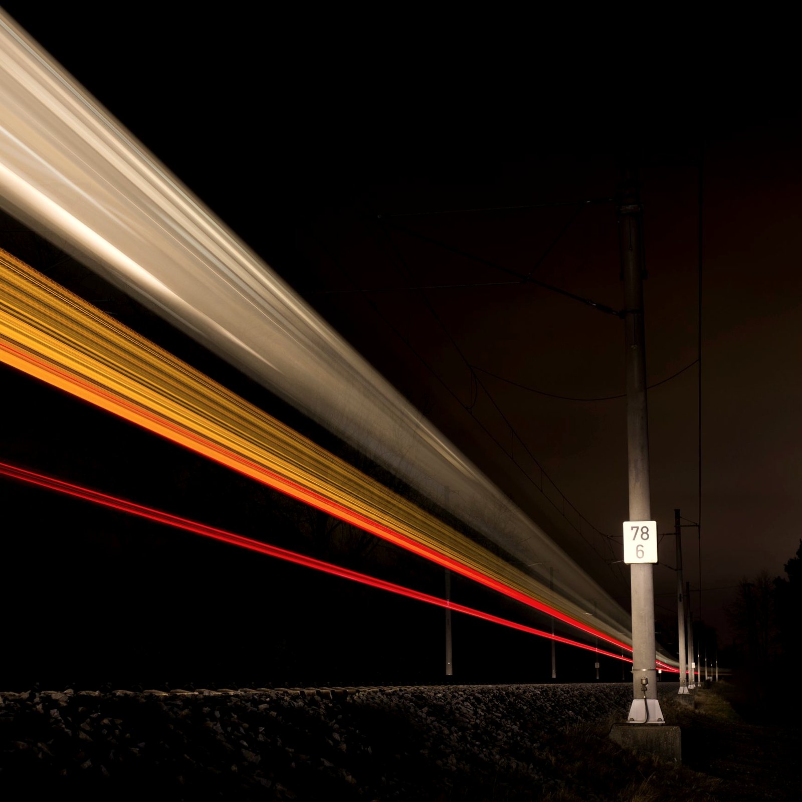 Long-exposure light trails of a train speeding along a rail line at night