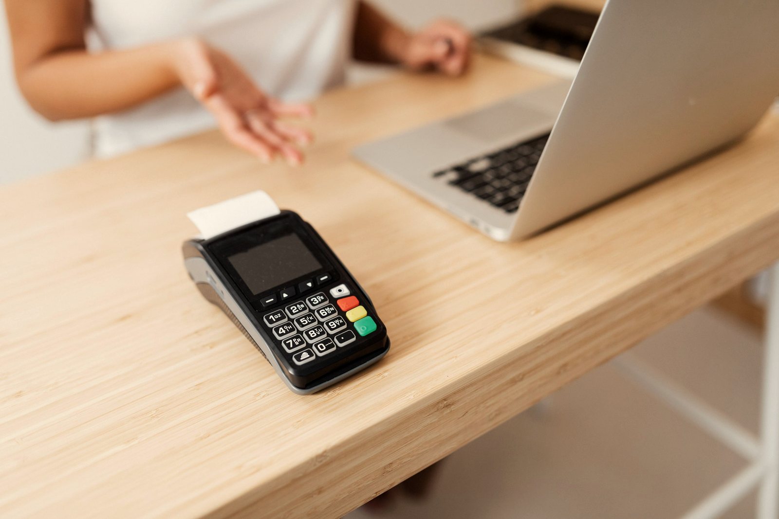 Card payment terminal on a wooden counter beside a laptop