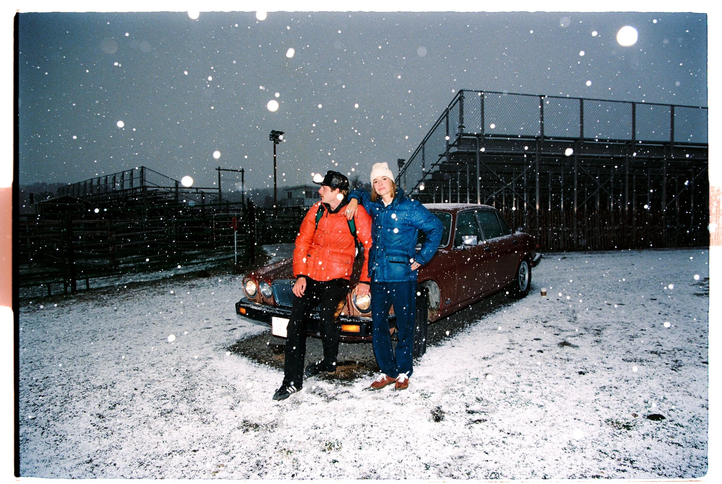 Two women in winter coats in front of a vintage car on a snowy day — CAO Winter 25