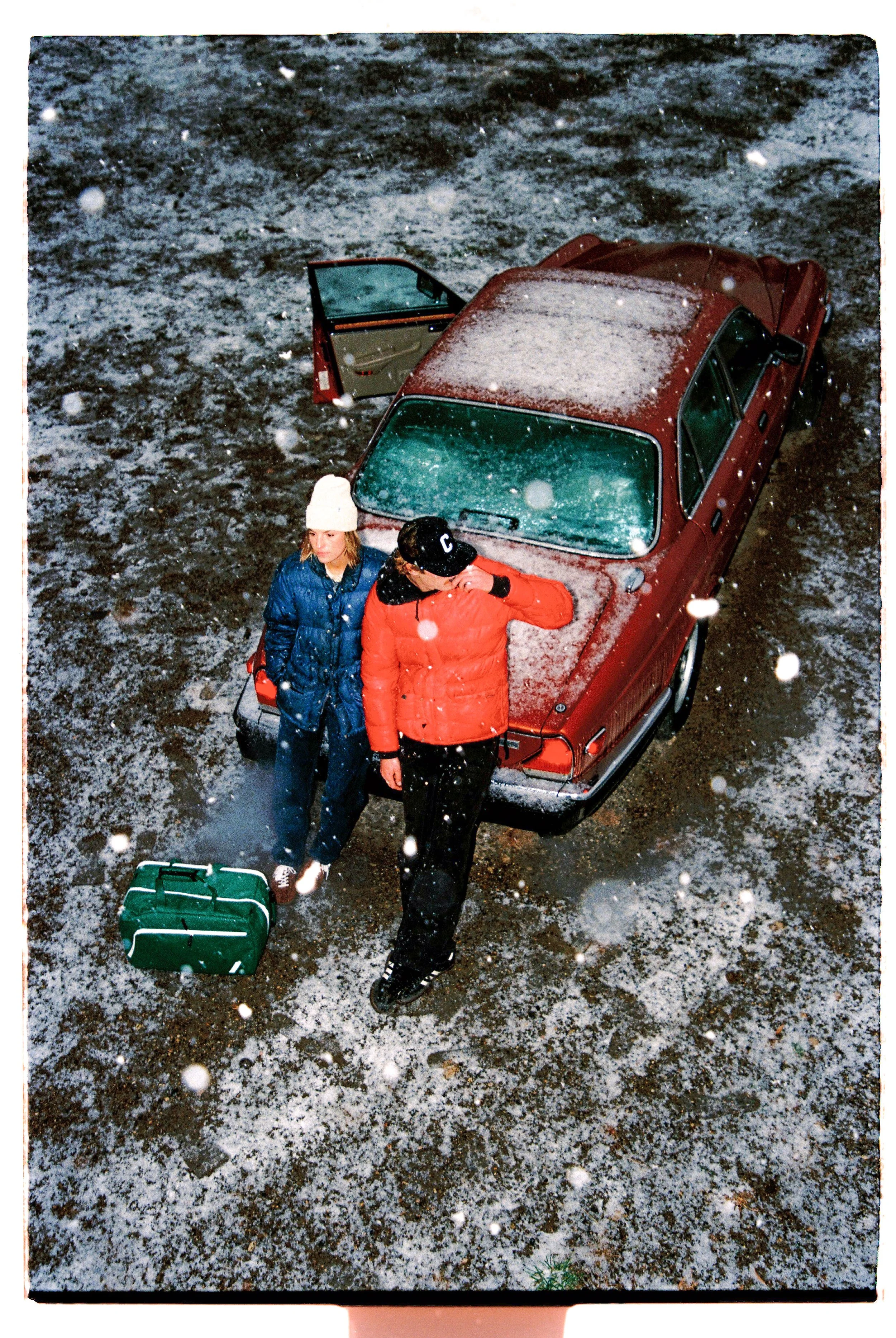 Two travelers next to a red car in light snowfall — CAO Winter 25