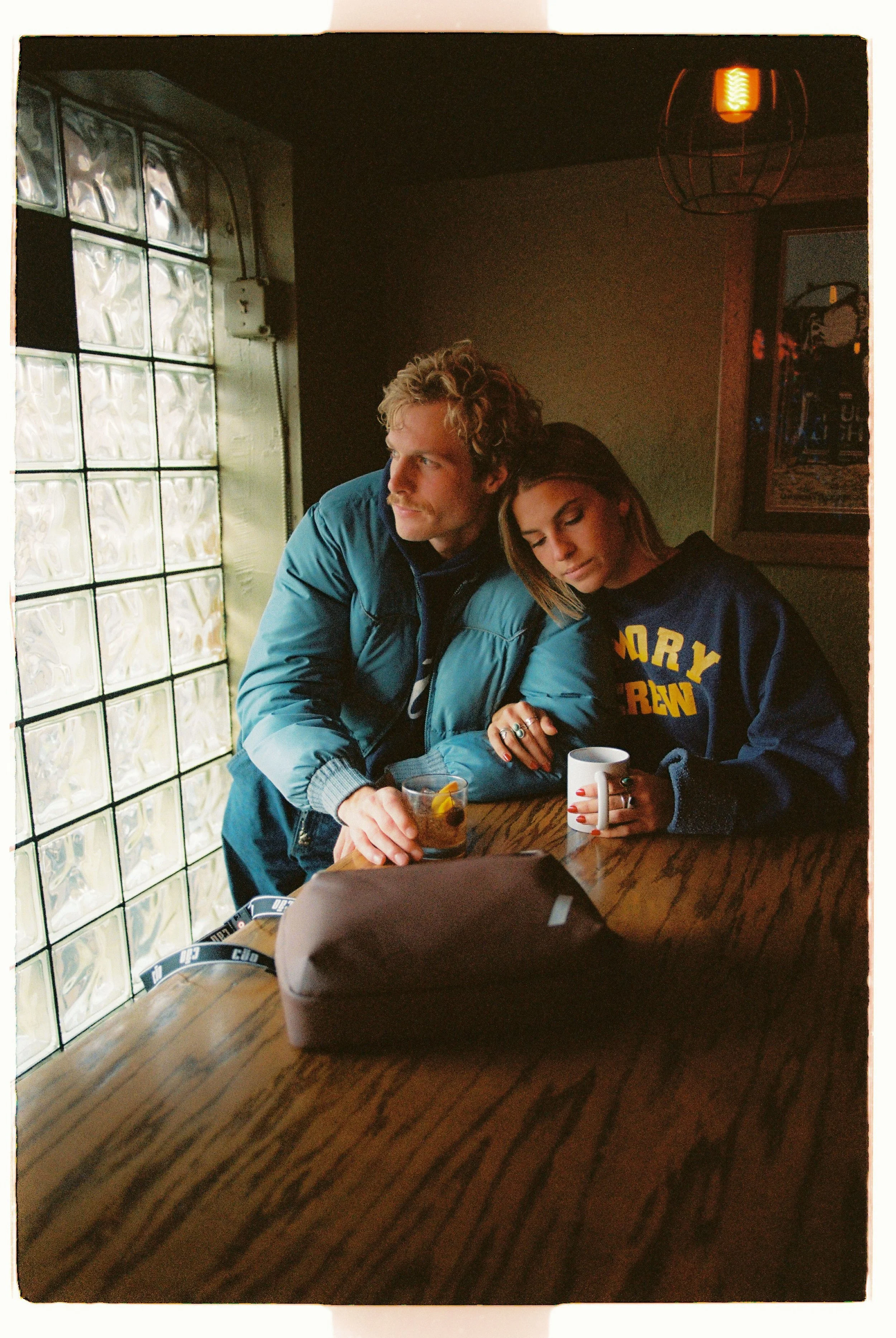 Couple sharing a drink at a wooden table in a dim café — CAO Winter 25