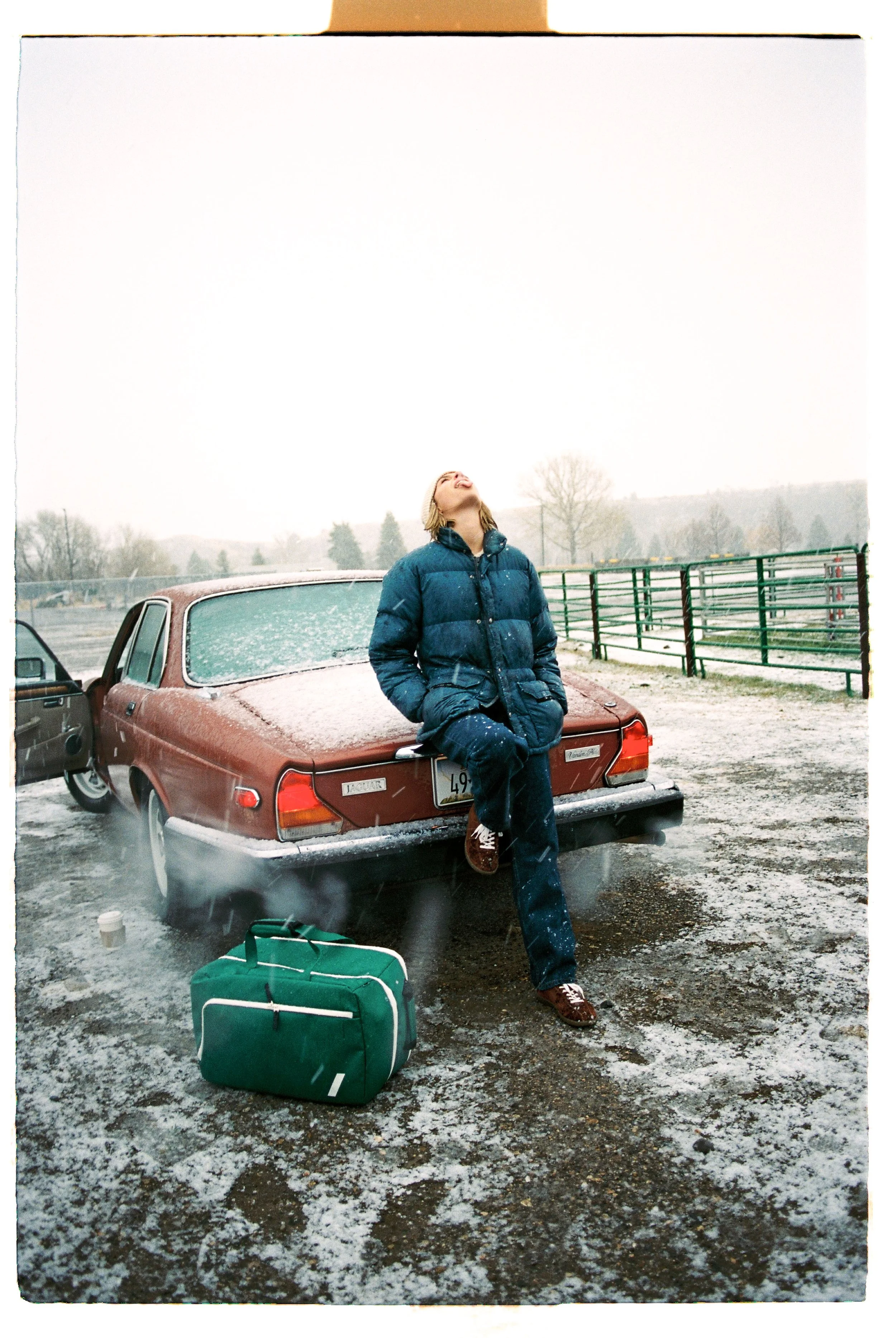 Traveler sitting on the trunk of a dusty red classic car in the snow — CAO Winter 25