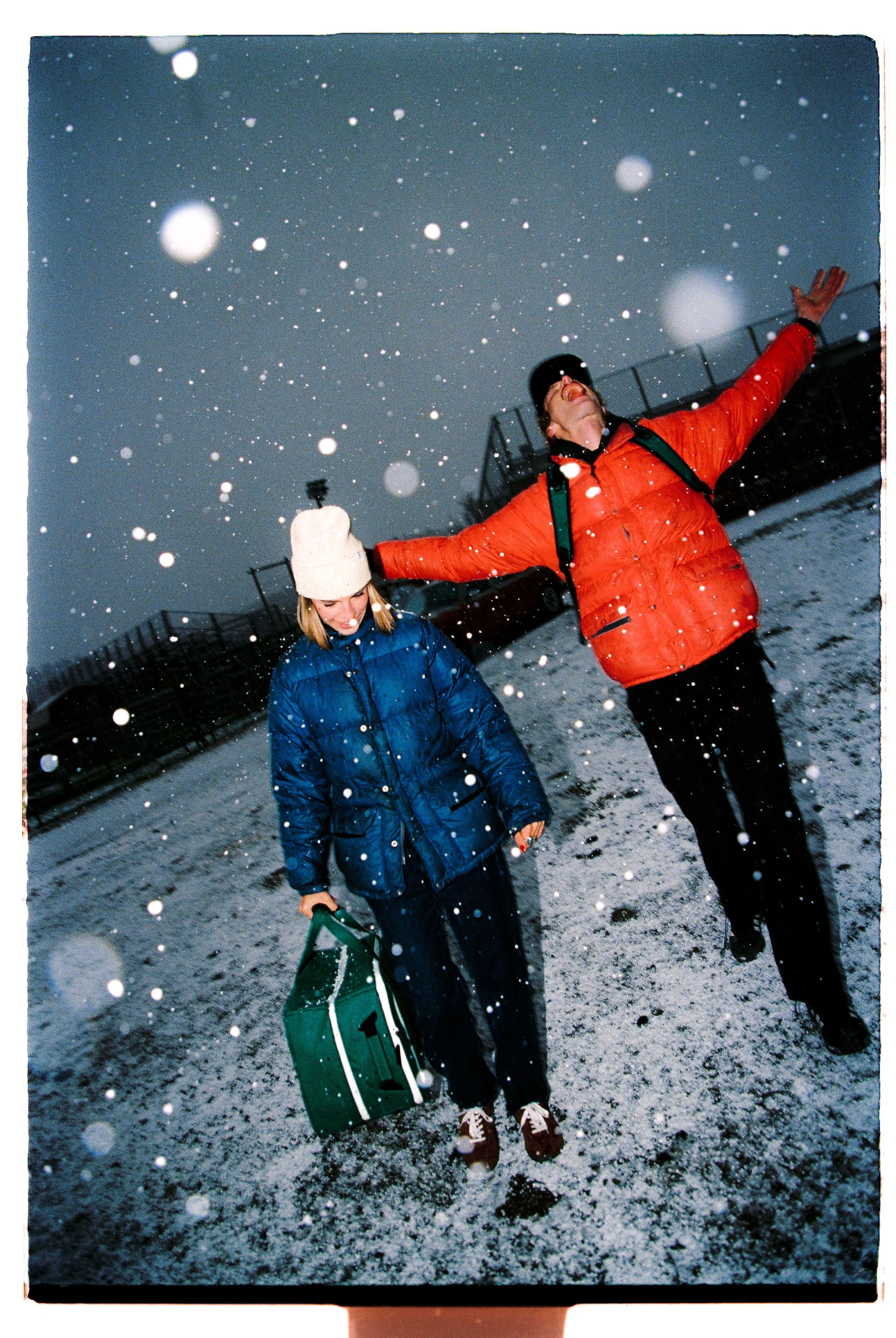 Couple laughing with arms outstretched in falling snow — CAO Winter 25