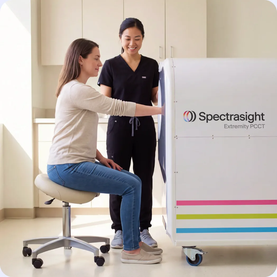 Clinician positioning a seated patient's arm in a Spectrasight Extremity PCCT scanner