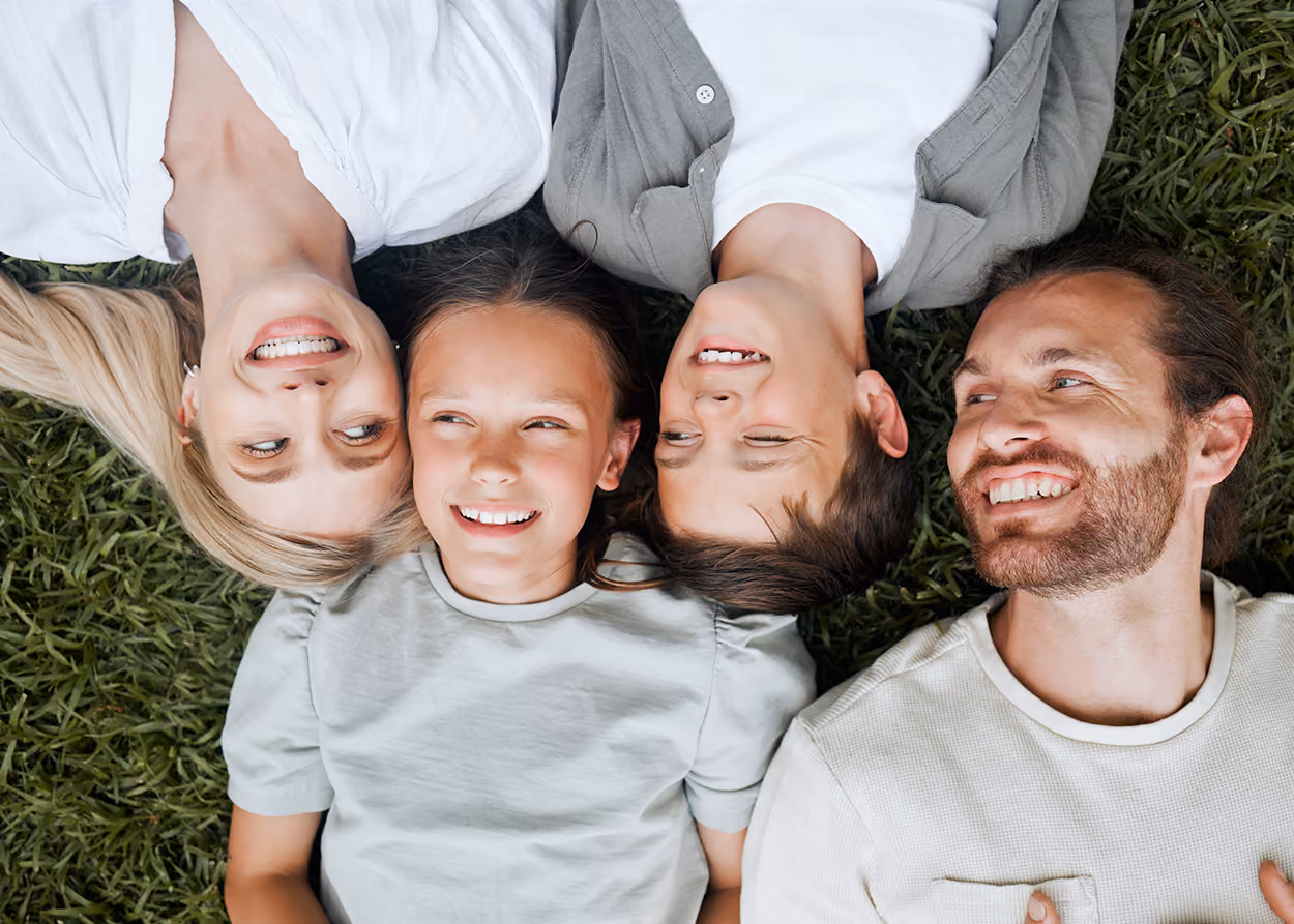 Smiling family of four lying on grass heads close together, including a man, woman, boy, and girl.
