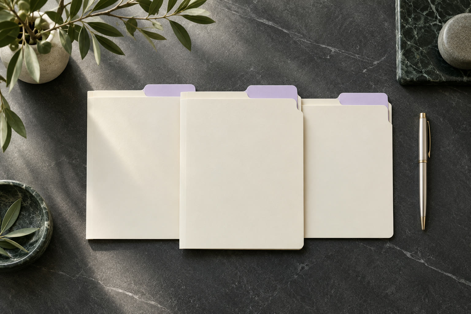 Three tabbed file folders and a pen laid out on a dark stone desk
