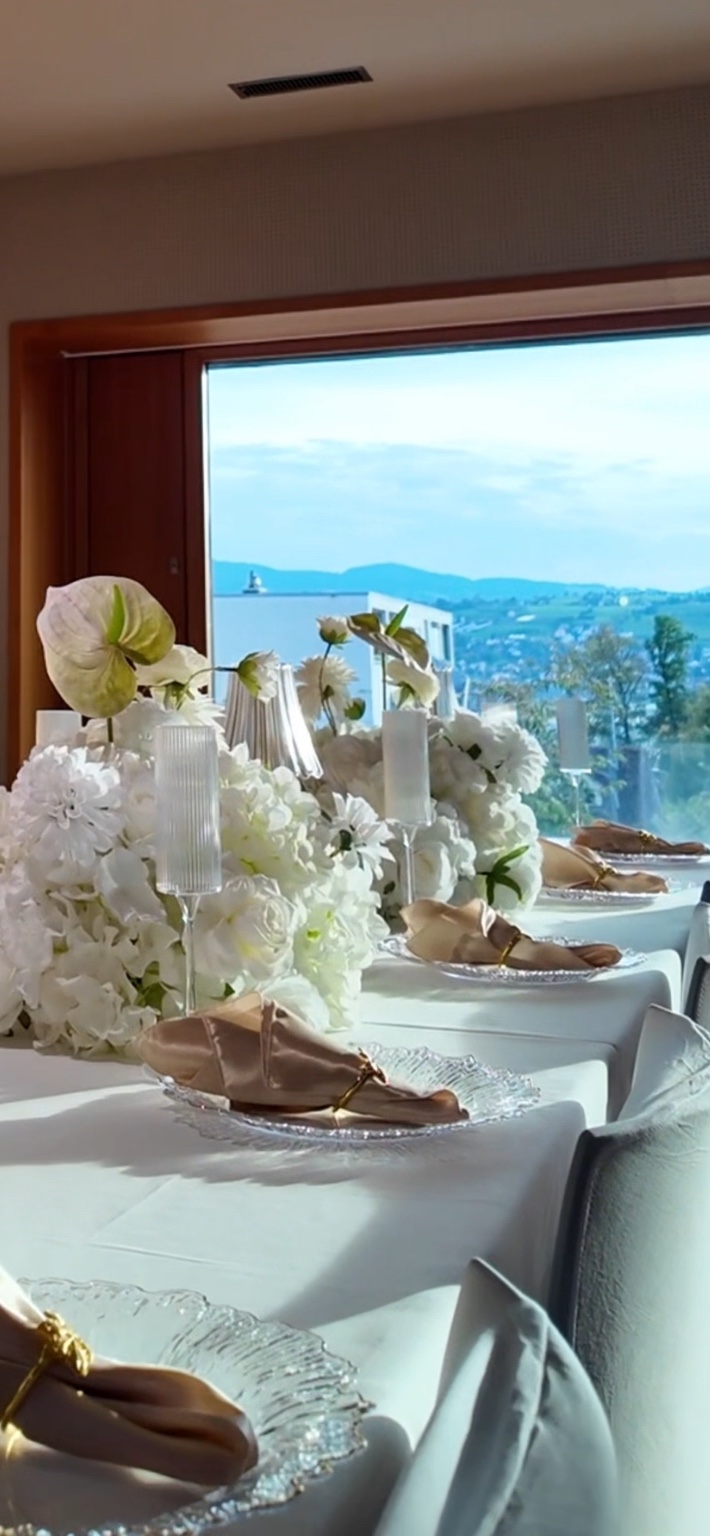 Helle Hochzeitstafel mit weissen Blumen, champagnerfarbenen Servietten und Seeblick.