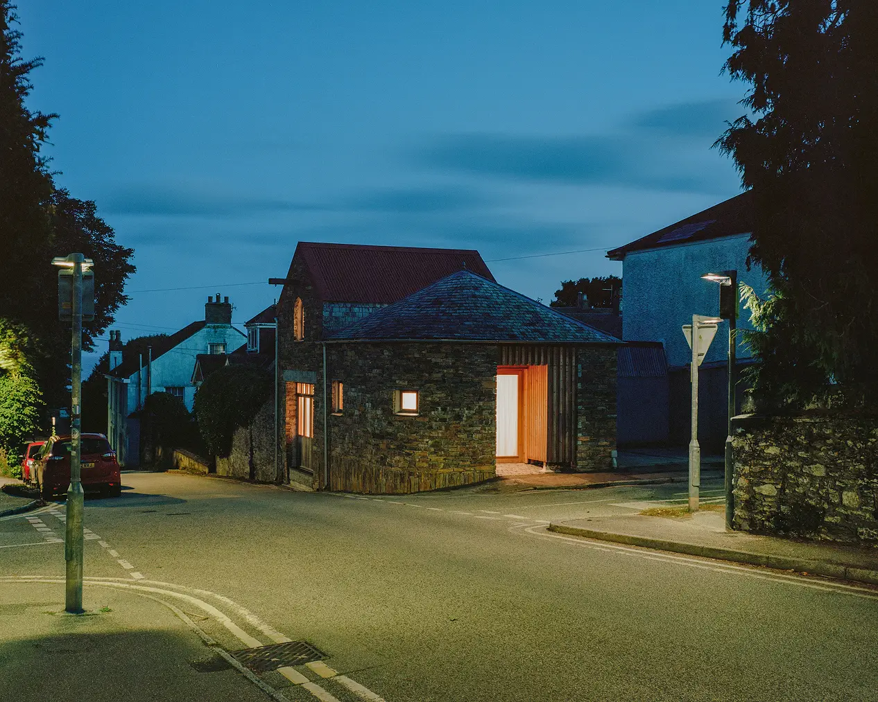 Converted stone barn with a red roof and timber door on a street corner