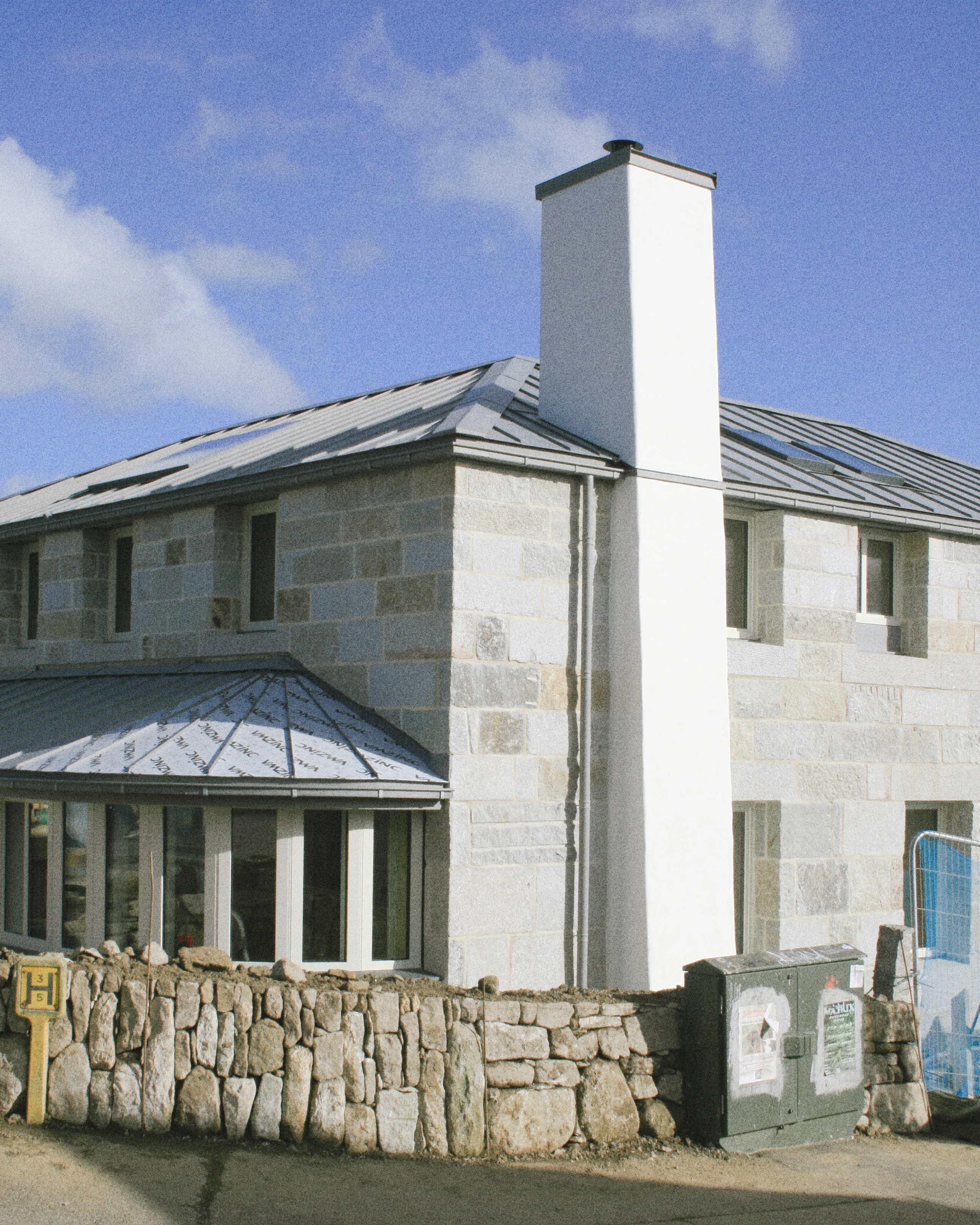 Converted stone barn with a red roof and timber door on a street corner