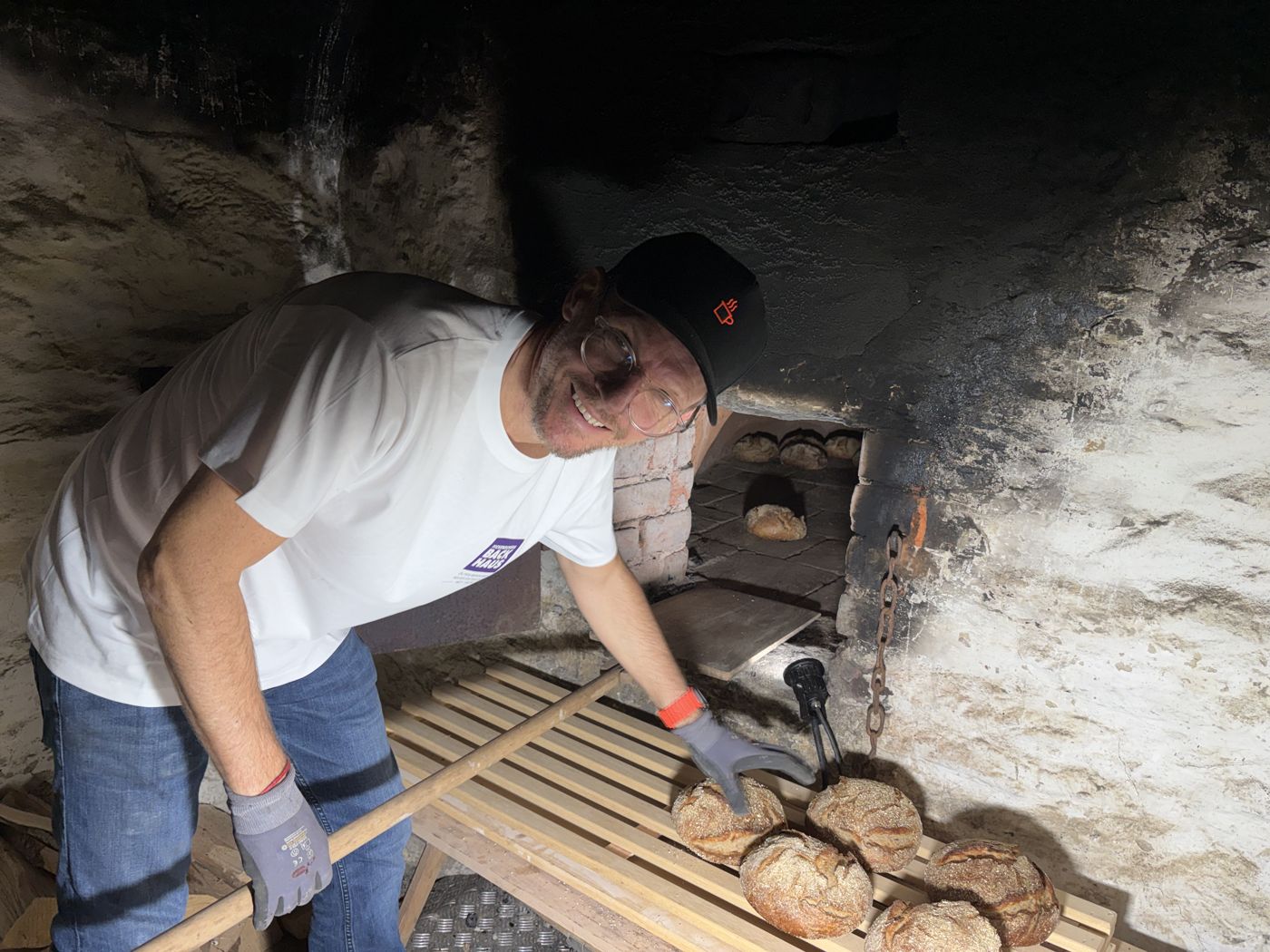 Ein Bäcker schießt Brote mit dem Holzschieber in den Holzbackofen ein