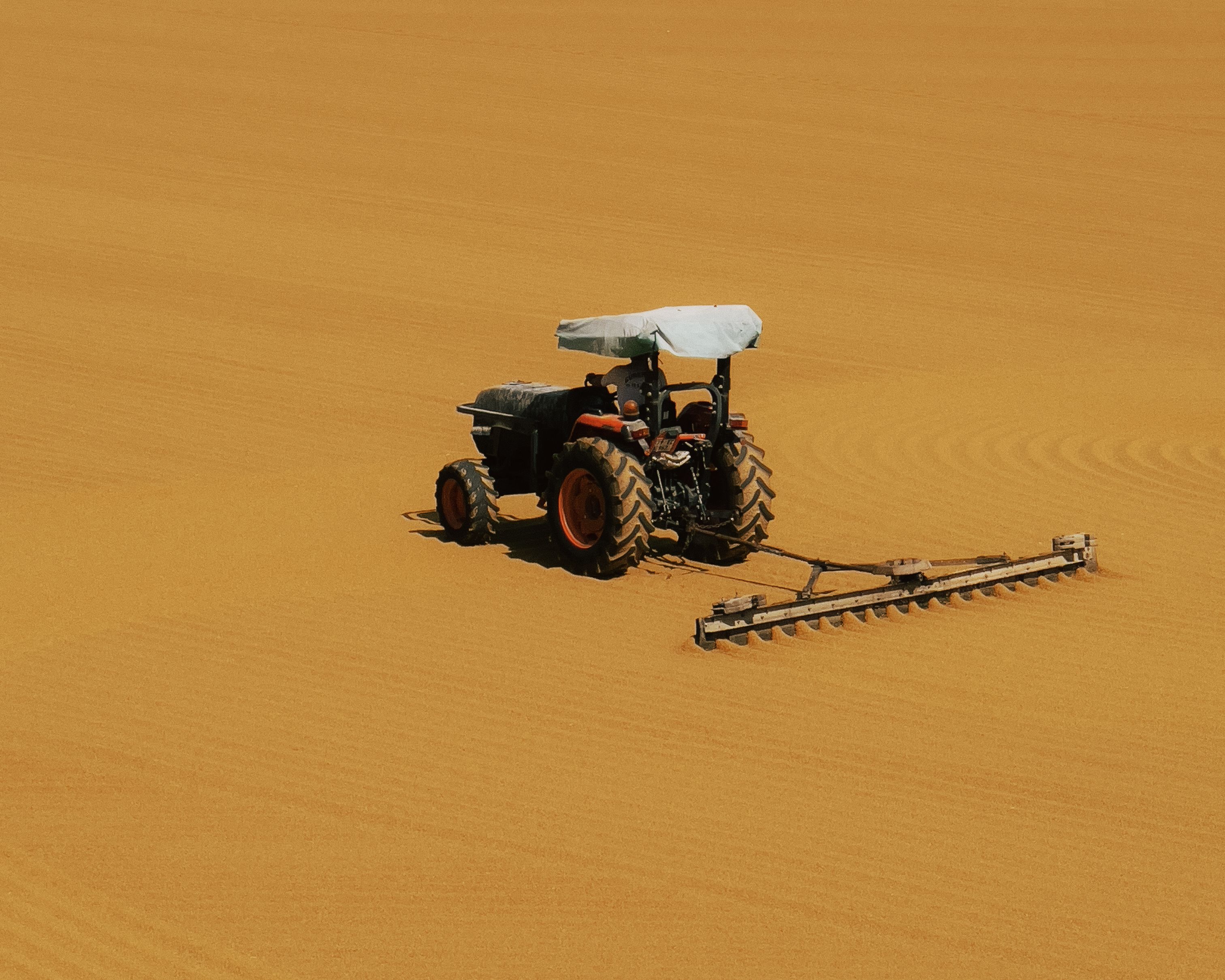 A tractor with a white canopy attachment at the rear is parked on an expansive field of golden soil.