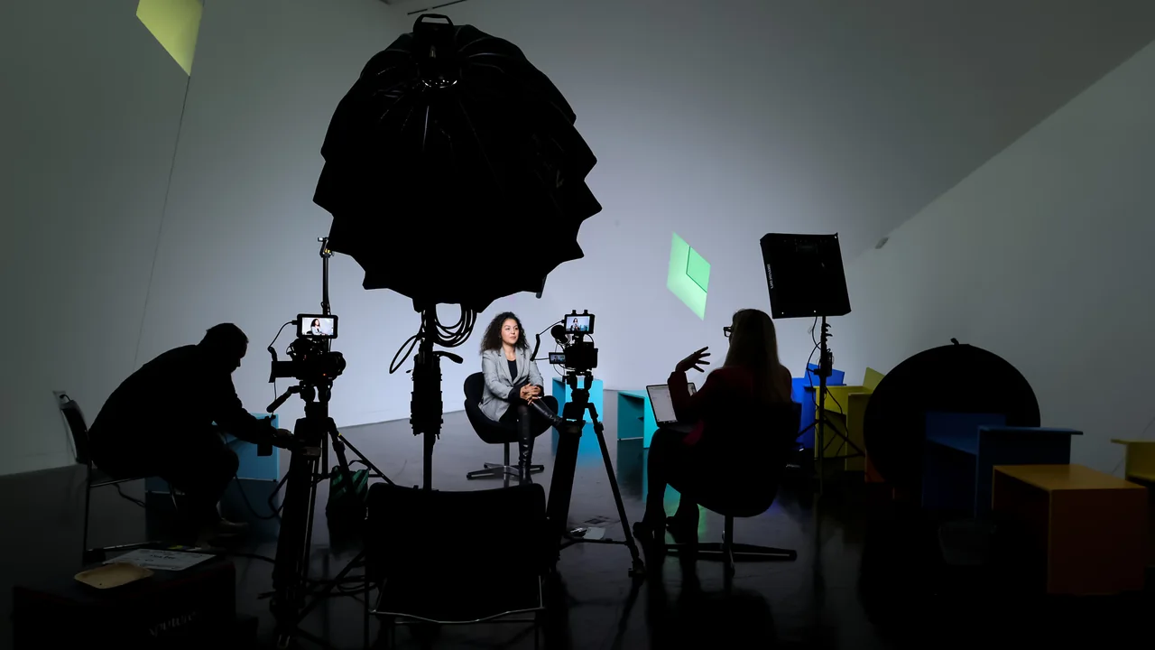 Silhouetted production crew and lighting equipment on a studio set.