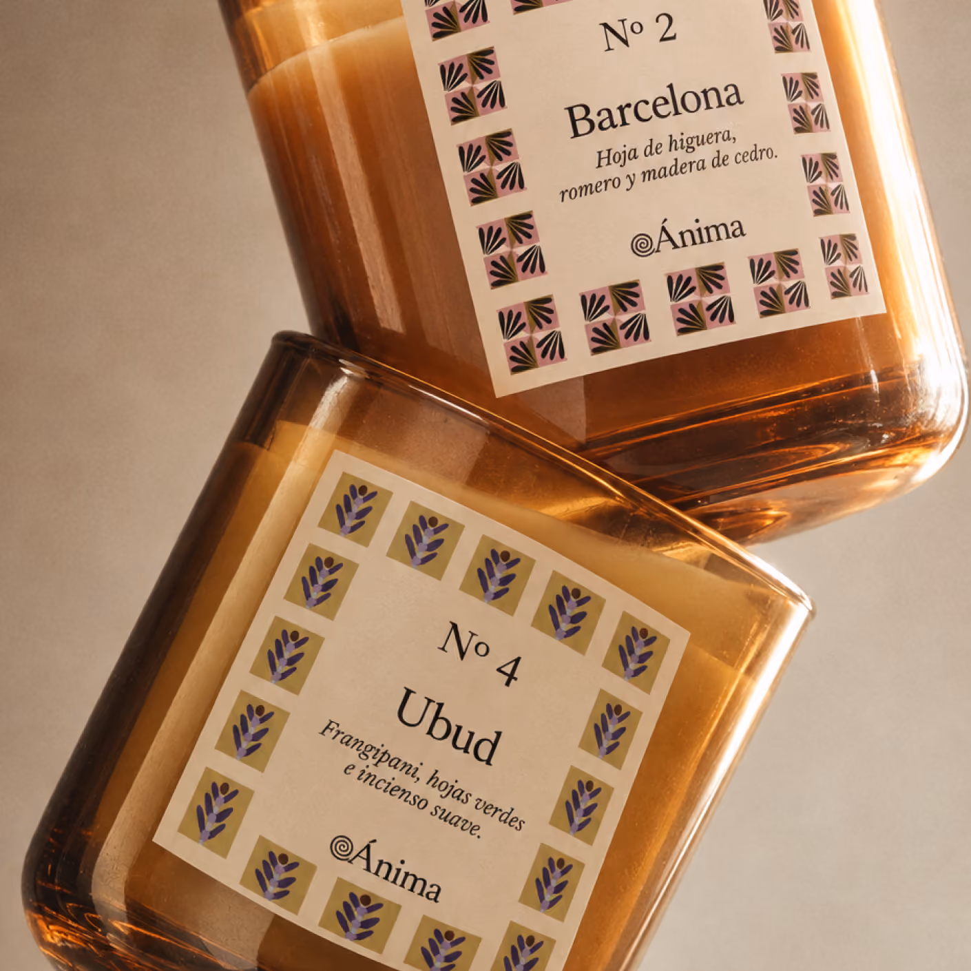 Dos velas de vidrio ámbar: No 2 Barcelona, con aroma de hoja de higuera, romero y madera de cedro, y No 4 Ubud, con aroma de frangipani, hojas verdes e incienso suave, ambas de Ánima.