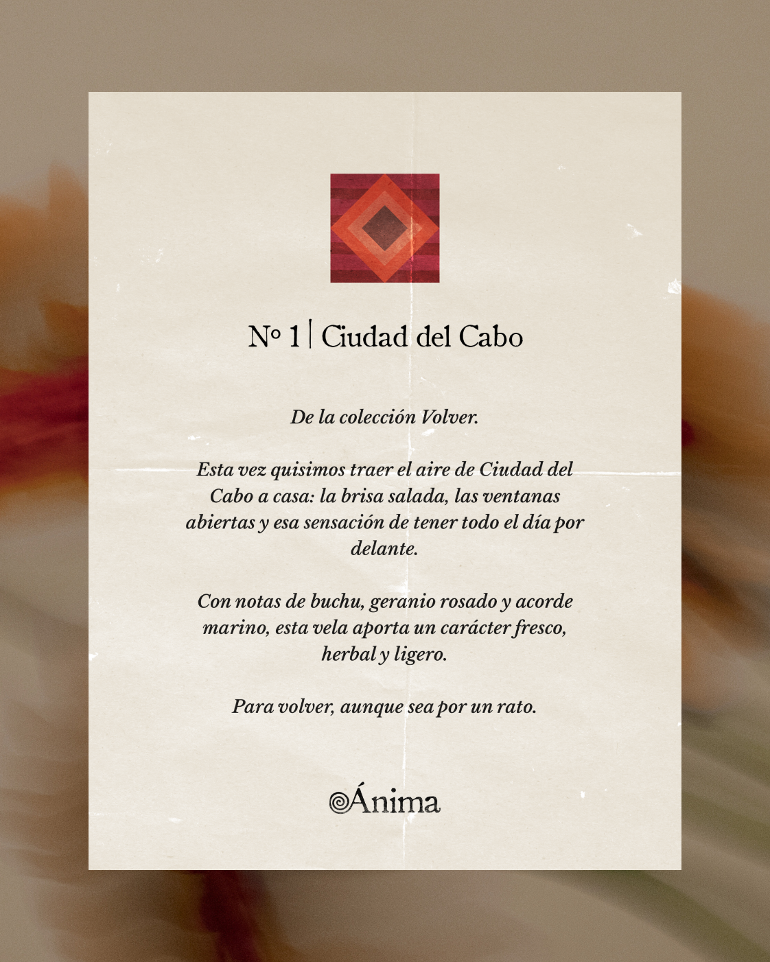 Text on a beige, slightly textured paper with a burgundy and orange geometric diamond logo at the top. The text reads: 'N° 1 | Ciudad del Cabo. De la colección Volver. Esta vez quisimos traer el aire de Ciudad del Cabo a casa: la brisa salada, las ventanas abiertas y esa sensación de tener todo el día por delante. Con notas de buchu, geranio rosado y acorde marino, esta vela aporta un carácter fresco, herbal y ligero. Para volver, aunque sea por un rato.' At the bottom is the brand name Ánima with a spiral design.