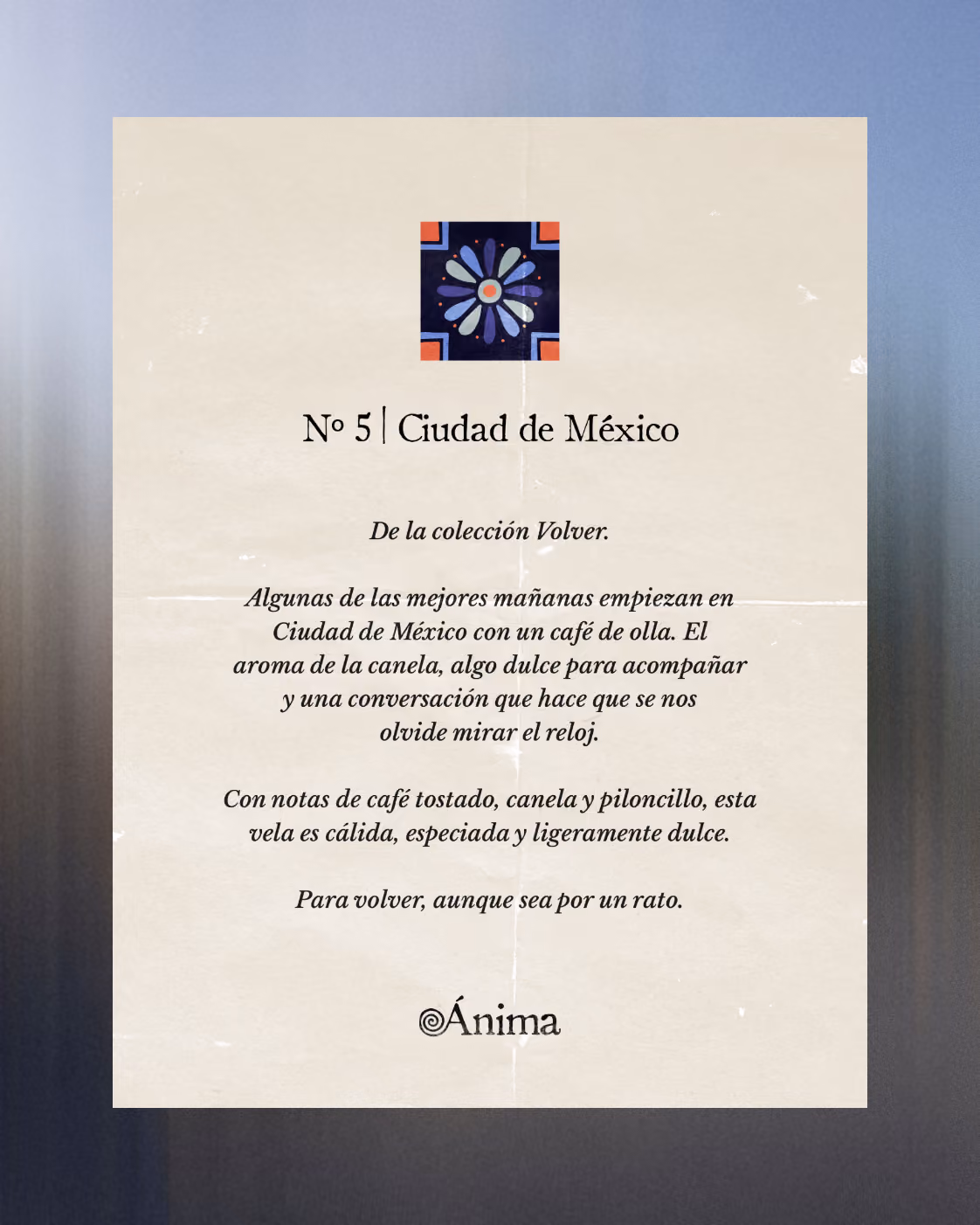 Papel color crema con un pequeño diseño floral de colores tipo azulejo en la parte superior central. Debajo, el texto dice: No 5 | Ciudad de México, y describe una vela de la colección Volver con notas de café tostado, canela y piloncillo. El texto evoca aromas cálidos, especiados y ligeramente dulces que recuerdan a un café de olla y a esos momentos en que olvidas mirar la hora. Al final aparece el nombre de la marca Ánima.