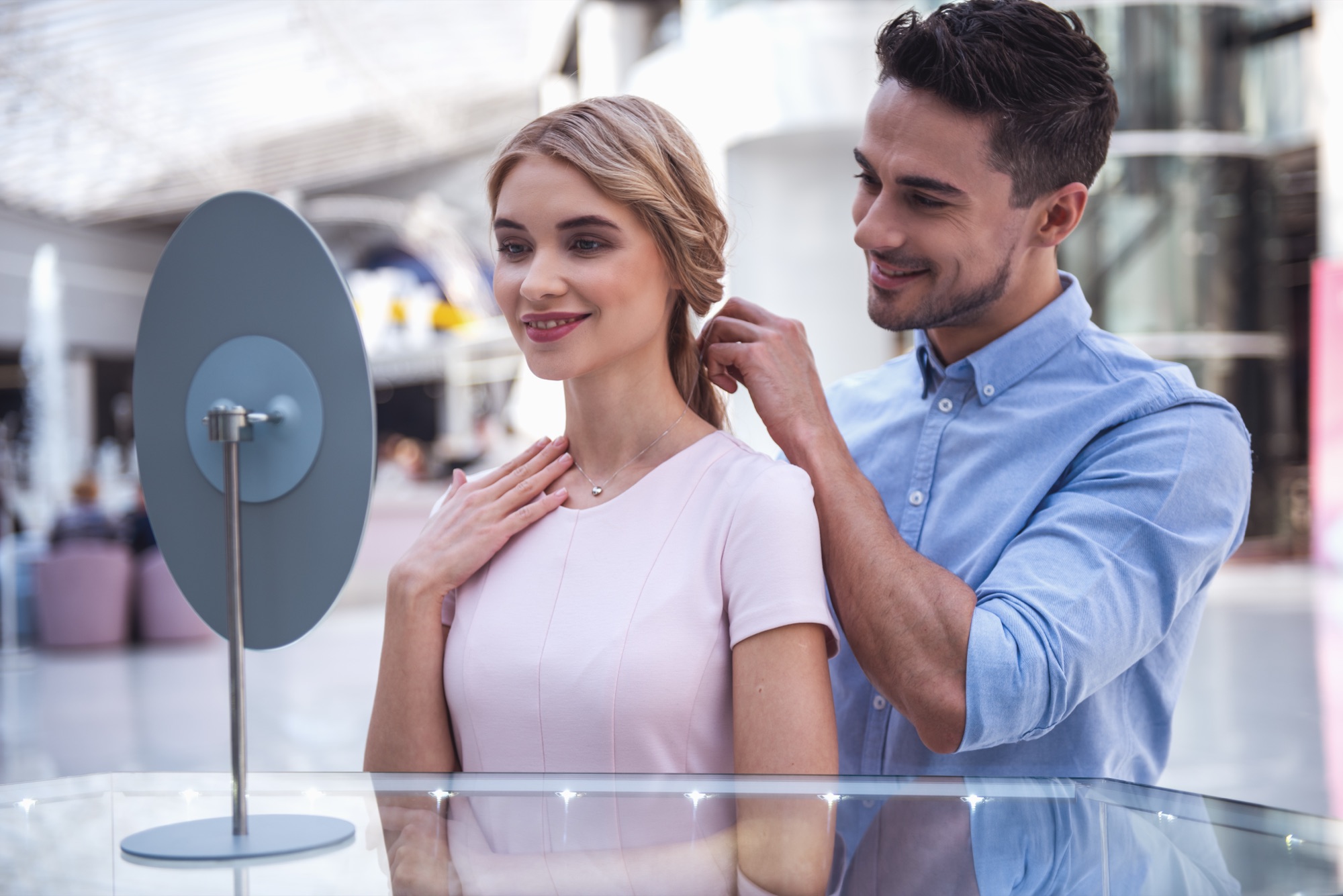 A man fastening a necklace on a smiling woman at a jewelry counter