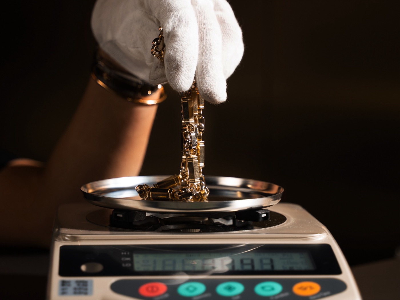 Gloved hand lowering a gold chain onto a calibrated jewelry scale