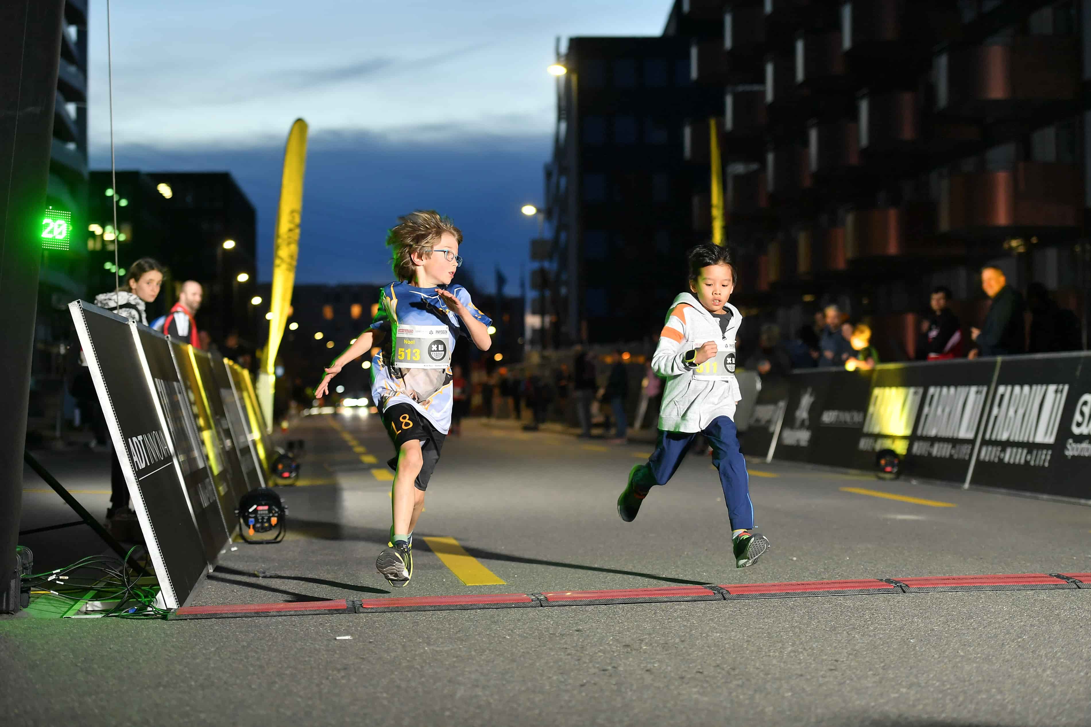 Kids Run beim NightRun Zürich, zwei Kinder sprinten im Abendlicht durch Dübendorf