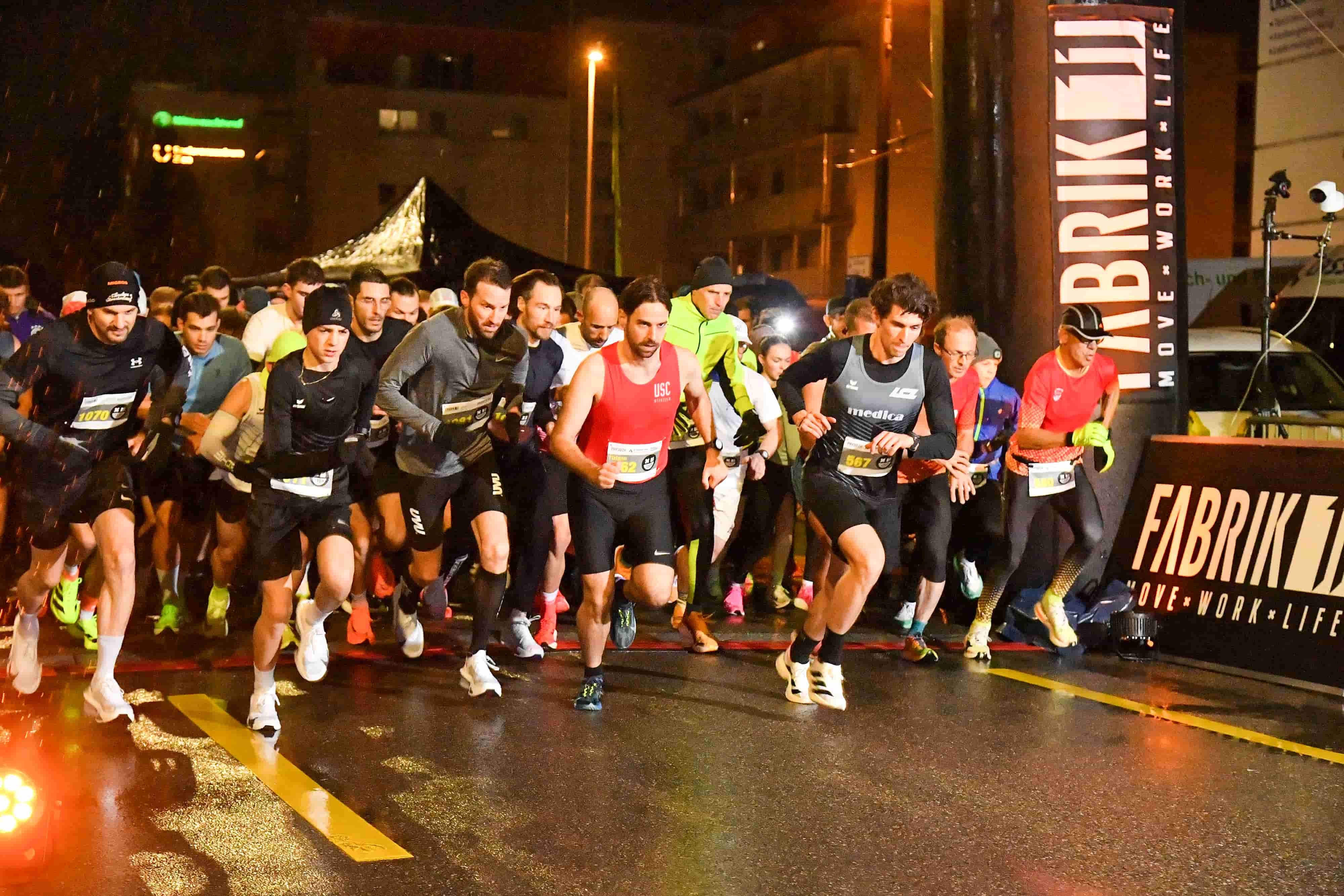 Event Infos zum NightRun Zürich: Startfeld im Regen vor dem FABRIK11 Banner in Dübendorf