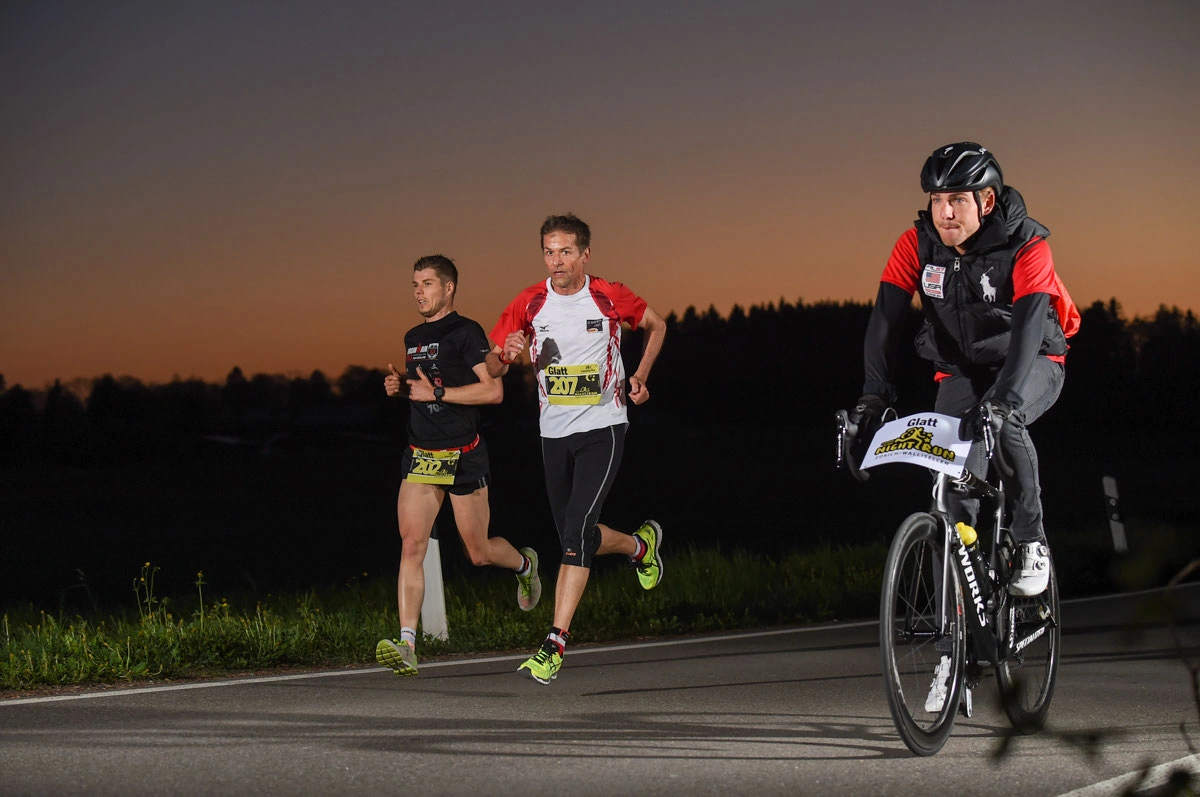 NightRun 2017 Wallisellen: Zwei Läufer und ein Radfahrer im Abendlicht