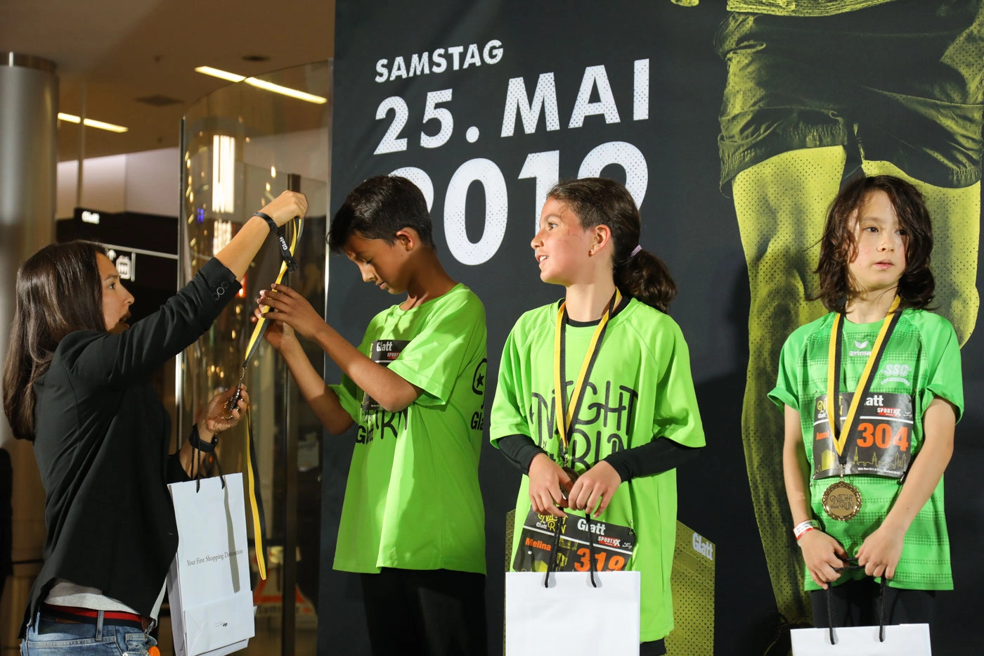 Glatt NightRun 2019: Kinder mit Medaillen bei der Siegerehrung vor der Glatt NightRun Wand