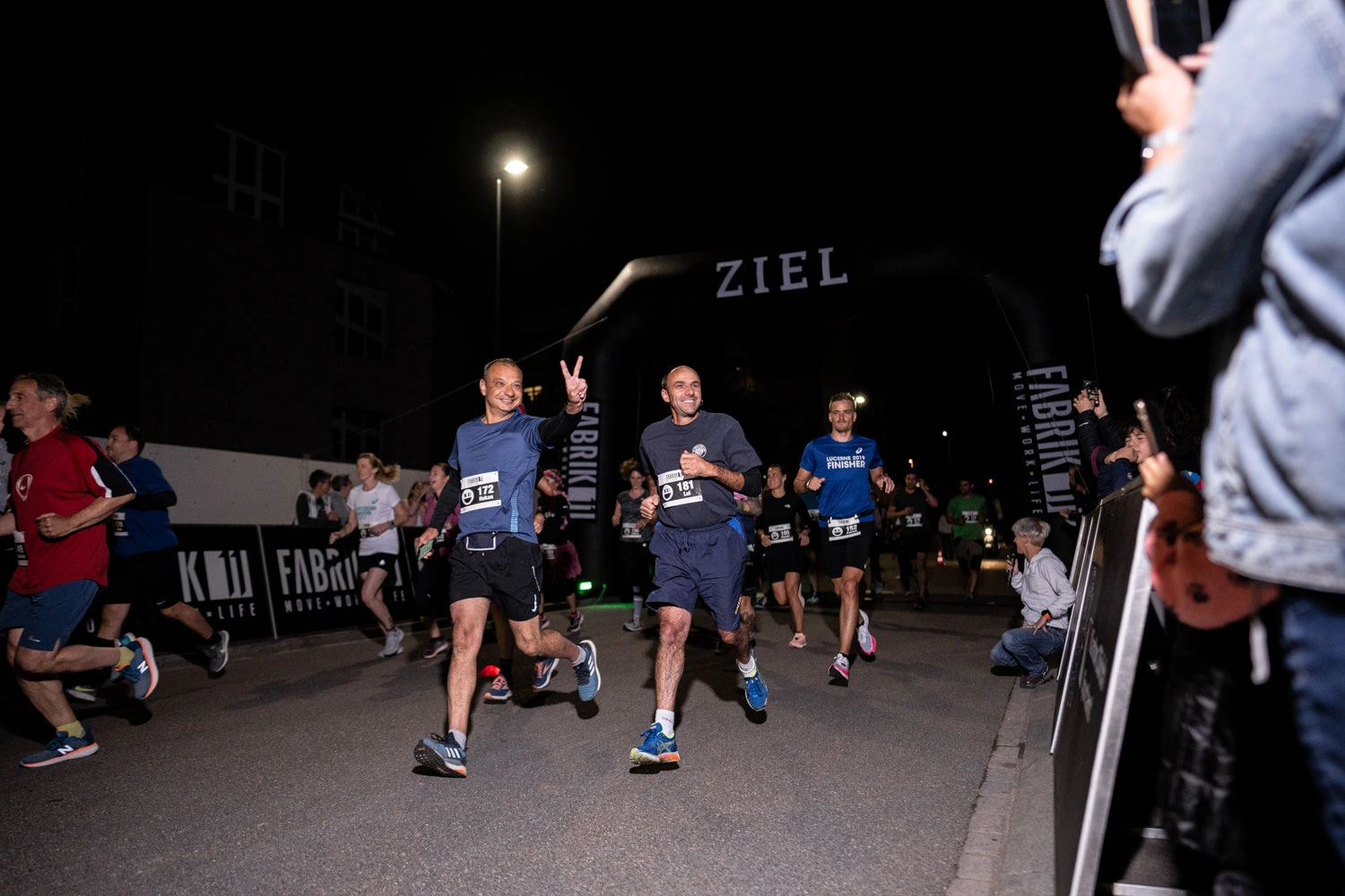 NightRun Dübendorf 2021: Läuferfeld auf der Zielgeraden unter dem Zielbogen