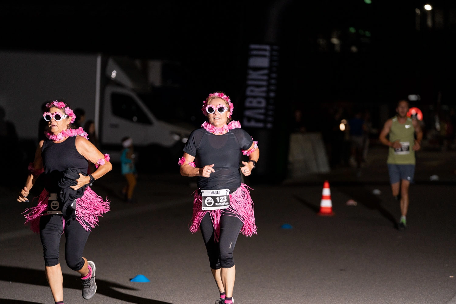 NightRun Dübendorf 2021: Zwei Läuferinnen mit pinken Accessoires laufen bei Nacht an Pylonen vorbei