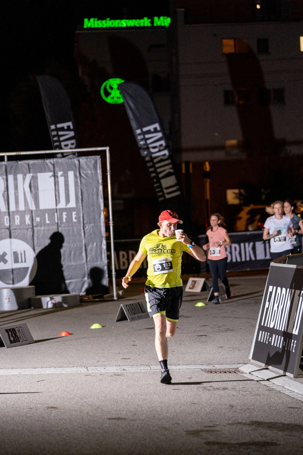 NightRun Dübendorf 2021: Läufer im gelben Shirt rennt ins Ziel vor dem FABRIK11 Banner