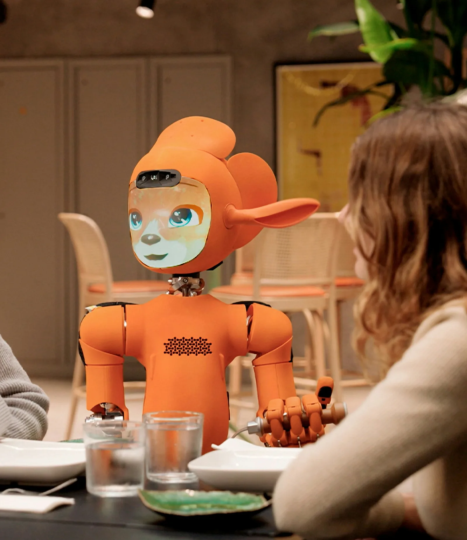 Robot humanoïde orange attablé face à une personne