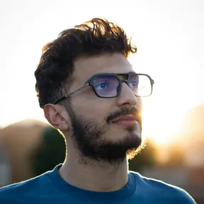 Portrait of a bearded man with glasses and a blue shirt, lit by warm sunset light