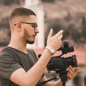 Man with glasses filming with a video camera on a tripod