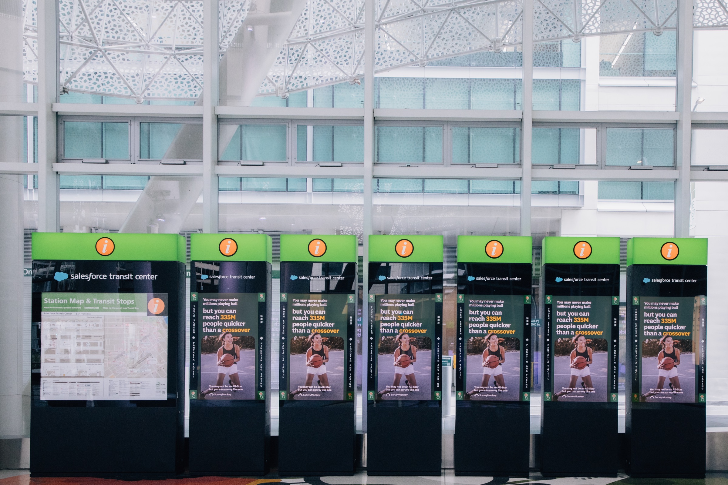 A row of Salesforce Transit Center wayfinding screens showing SurveyMonkey ads