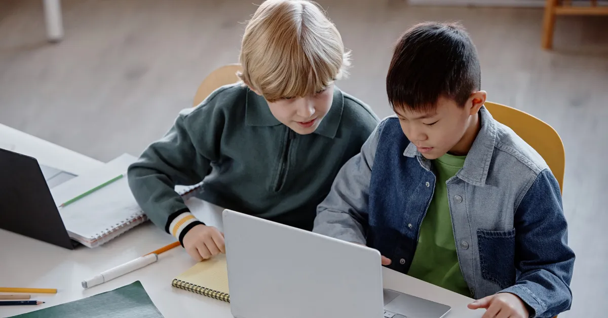 Two students working together on laptops in a classroom