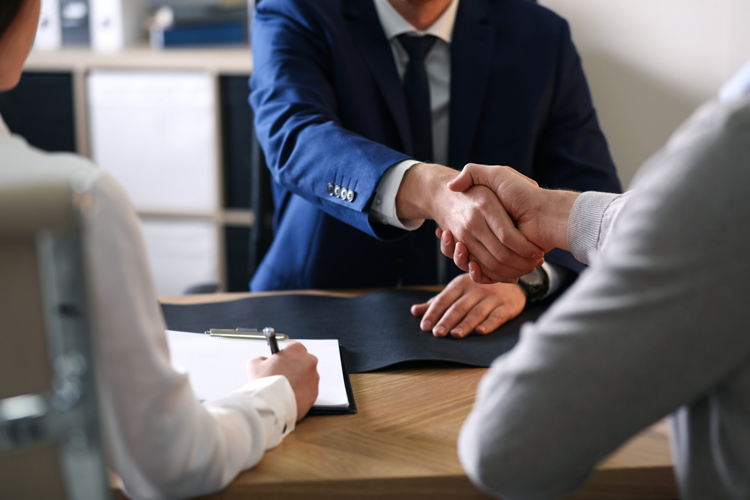Two people shaking hands across a desk after agreeing on a plan