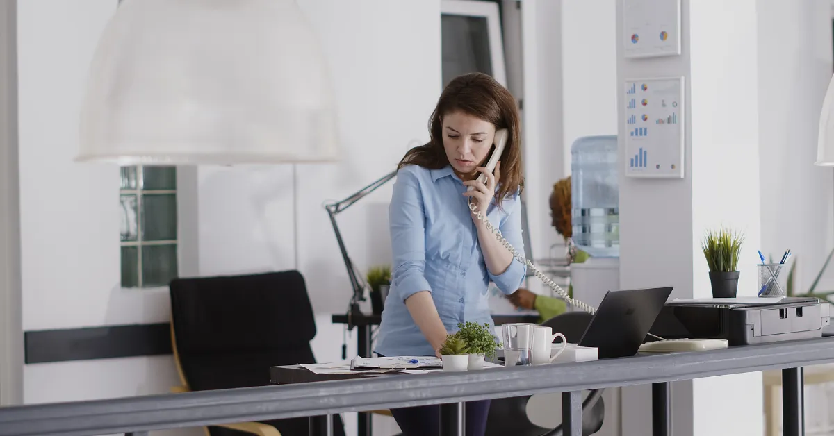 A staff member answering a desk phone in a bright office