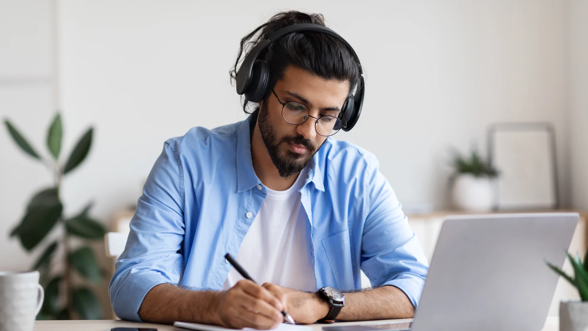 A student with headphones taking notes while studying the Illinois public adjuster online course on a laptop