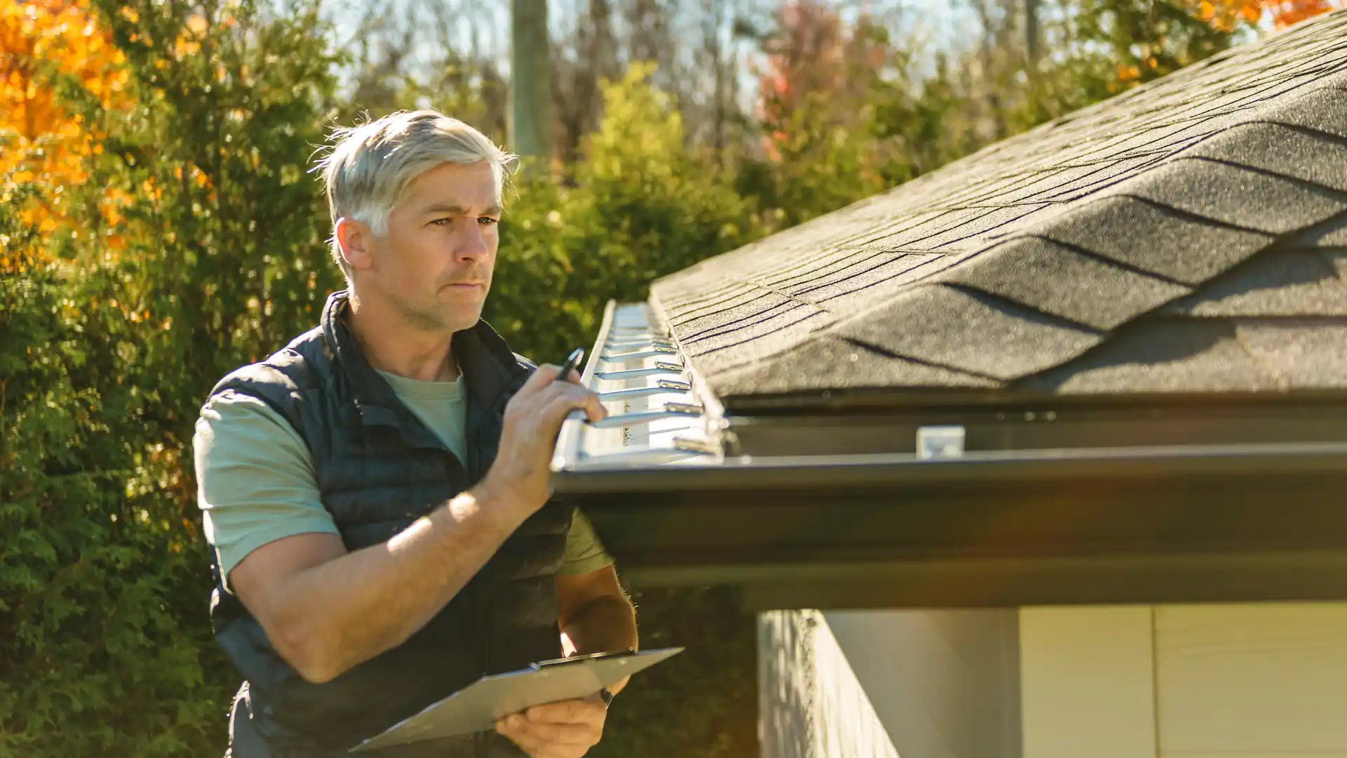 Public adjuster checking a home's roof gutter and noting the damage on a clipboard